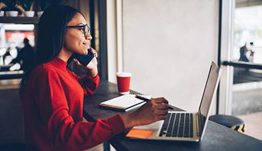 Woman account manager talking on the phone while working on her laptop in a remote location