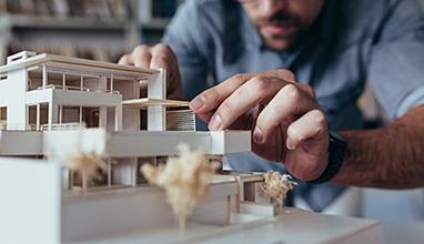 Close up of male architect hands making model house. Man architect working in the office.