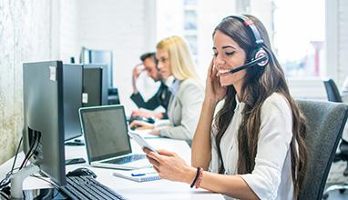 Friendly female customer support operator with headset using phone in office