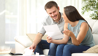 Happy couple reading mail and checking accountancy looking each other sitting on a couch at home