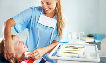 A young girl being prepped for a dental appointment by a pretty nurse