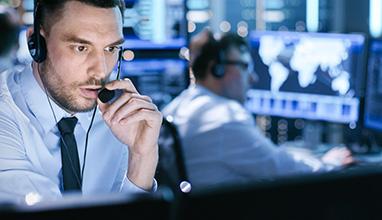 In Monitoring Room Technical Support Specialist Speaks into Headset. His Colleagues are Working in the Background.