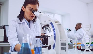 Important research. Serious experienced scientist working with her microscope and wearing a uniform