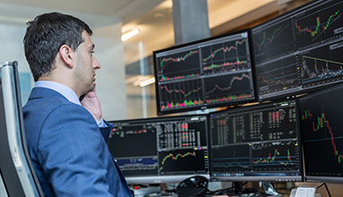 Male stockbroker watching charts and data analyses on multiple computer screens