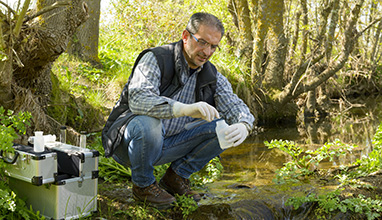 Man collecting water samples from a stream in the forest