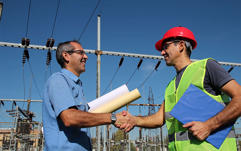 Smiling workers with blueprints and clipboard in meeting at electrical substation.