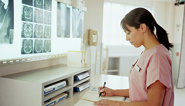 Serious woman nurse looking at form in front of x-ray scans