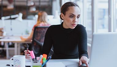 Image of young woman working on laptop while sitting at her desk in modern office. African female executive at work.