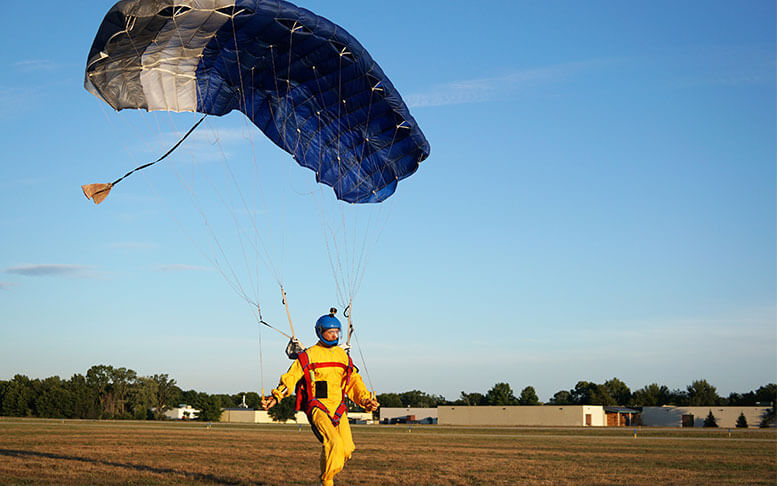 Skydiver under a small blue canopy of a parachute is landing on airfield, close-up.