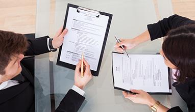 Businessman and businesswoman talking while holding resumes at a table while