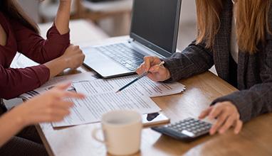 Group of businesswoman discussing documents at a table with a calculator and a laptop