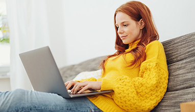 Woman in yellow sweater writing her resume on a laptop 