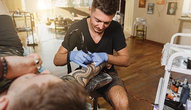 A male tattoo artist tattooing a mans arm in a tattoo studio