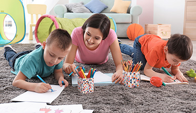 Woman nanny coloring with two boys on the floor of a house