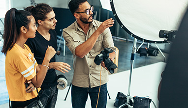 A man photographer holding a camera giving directions to two other workers in a photography studio.