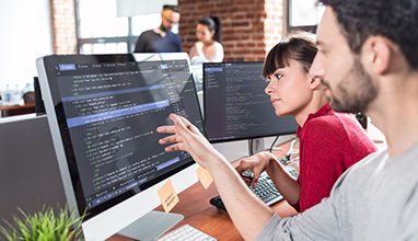 Man and woman looking at code on a computer in an office