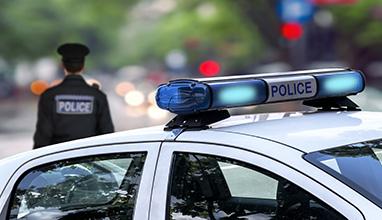 Male police officer standing behind a patrol car