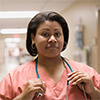 Woman wearing medical scrubs and a stethoscope around her neck at a hospital hallway
