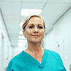 Woman wearing medical scrubs holding a clip board in a hospital hallway